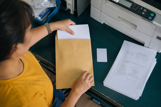 Hands organizing an envelope and papers at a photocopy counter